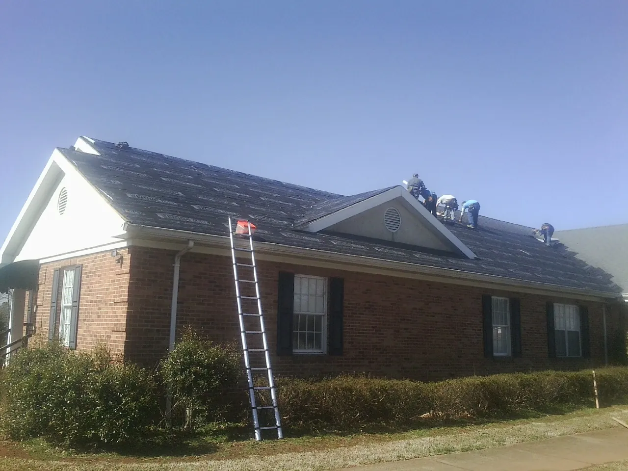 Crew tearing shingles off a brick ranch roof with a ladder set — Emergency Roof Repair work by our crew in Queenstown