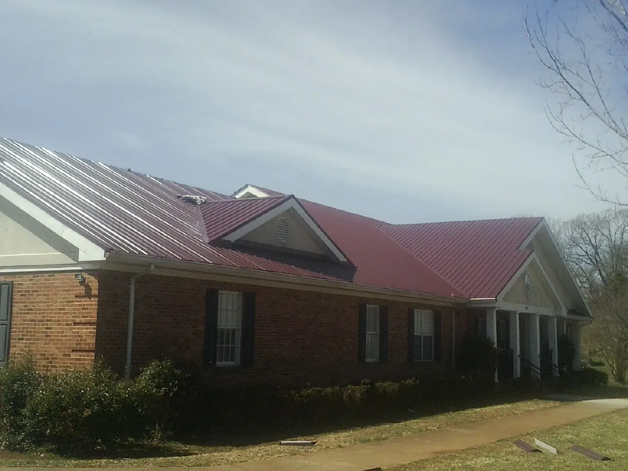Red metal roof with gabled entries on a long brick building, from a Hail Damage Roof Repair job in Queenstown